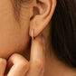 A close-up, profile view of a person’s ear wearing a small, thin silver huggie hoop earring. The earring is embellished with a row of tiny, shimmering cz stones along its outer edge. Dainty and elegant jewellery gift for her