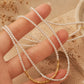 Hand holding a beaded choker necklace with gold and silver beads against a beige background.