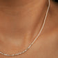 Close-up of a woman wearing a delicate, minimalist choker necklace made of tiny white glass pearls and a textured row of shimmering sterling silver nuggets.