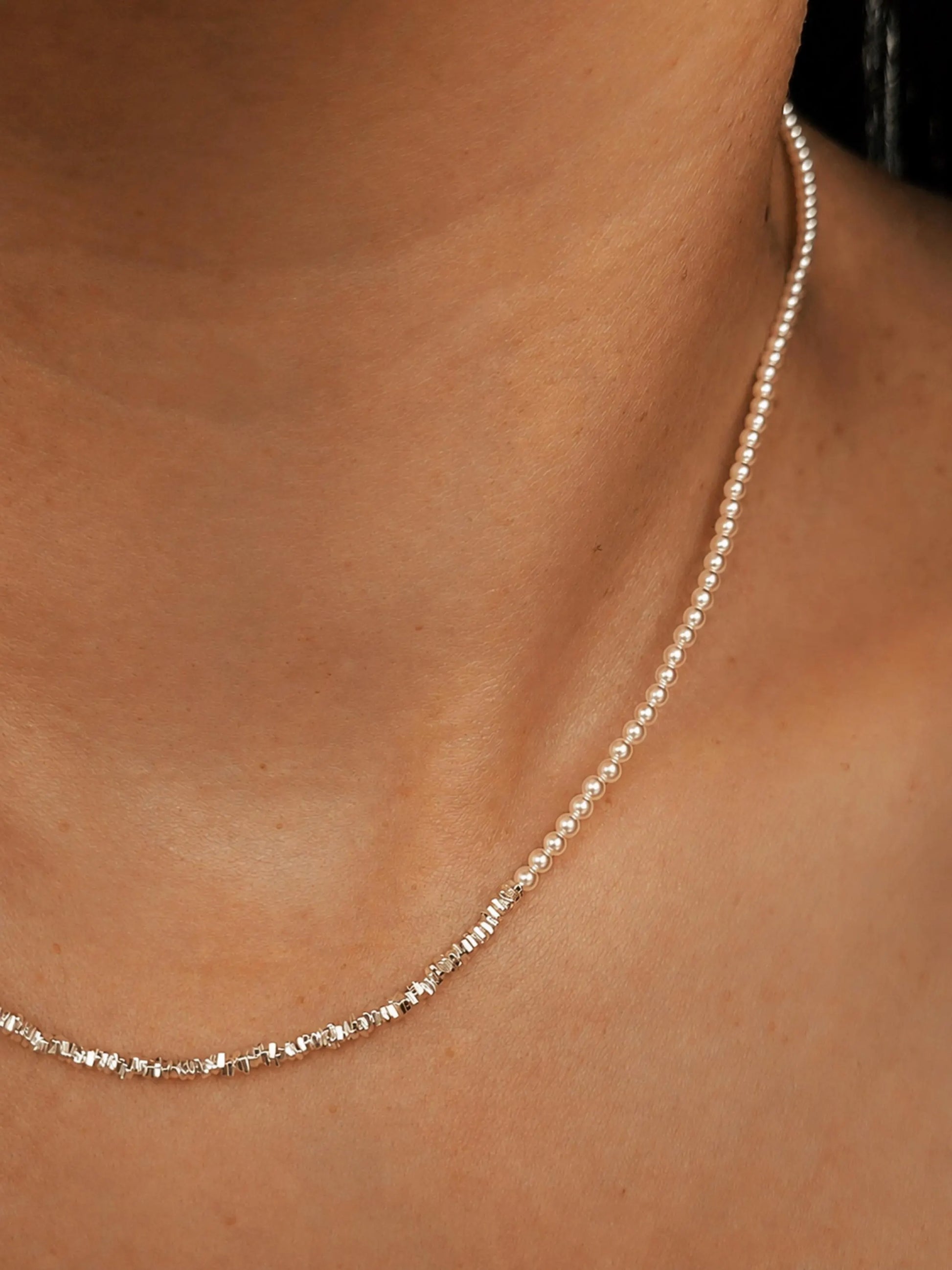 Close-up of a woman wearing a delicate, minimalist choker necklace made of tiny white glass pearls and a textured row of shimmering sterling silver nuggets.