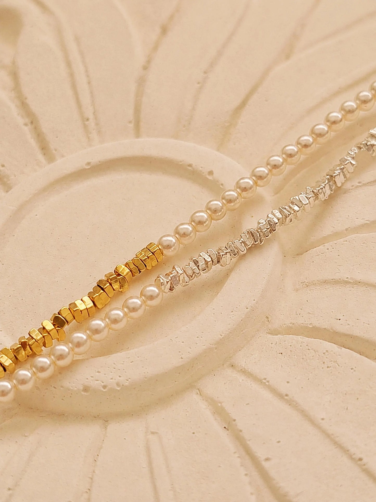 Two dainty 2mm glass pearl choker necklaces displayed on a decorative stone tile, one featuring textured 18k gold-plated nuggets and the other with sterling silver nuggets.