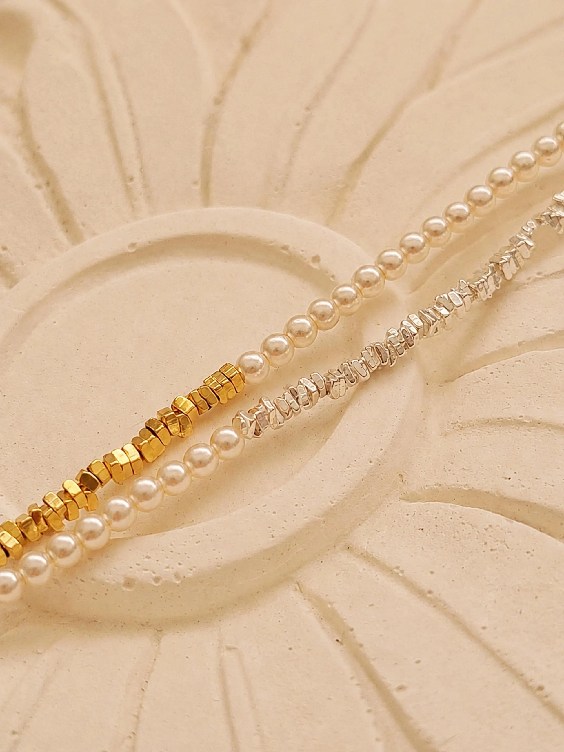 Two dainty 2mm glass pearl choker necklaces displayed on a decorative stone tile, one featuring textured 18k gold-plated nuggets and the other with sterling silver nuggets.