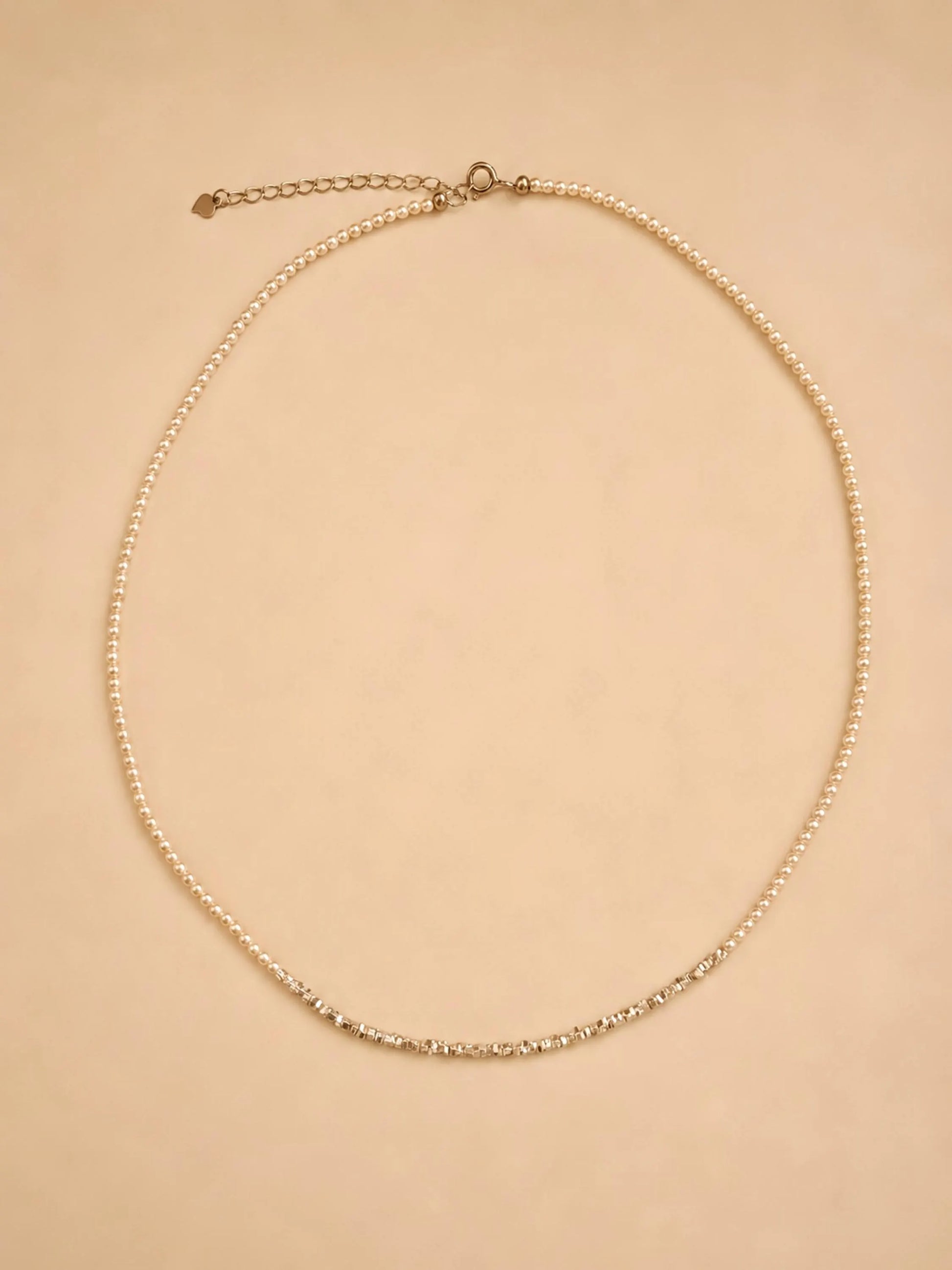 A dainty 2mm glass pearl choker necklaces displayed on a luxury beige color surface featuring textured sterling silver nugget beads.