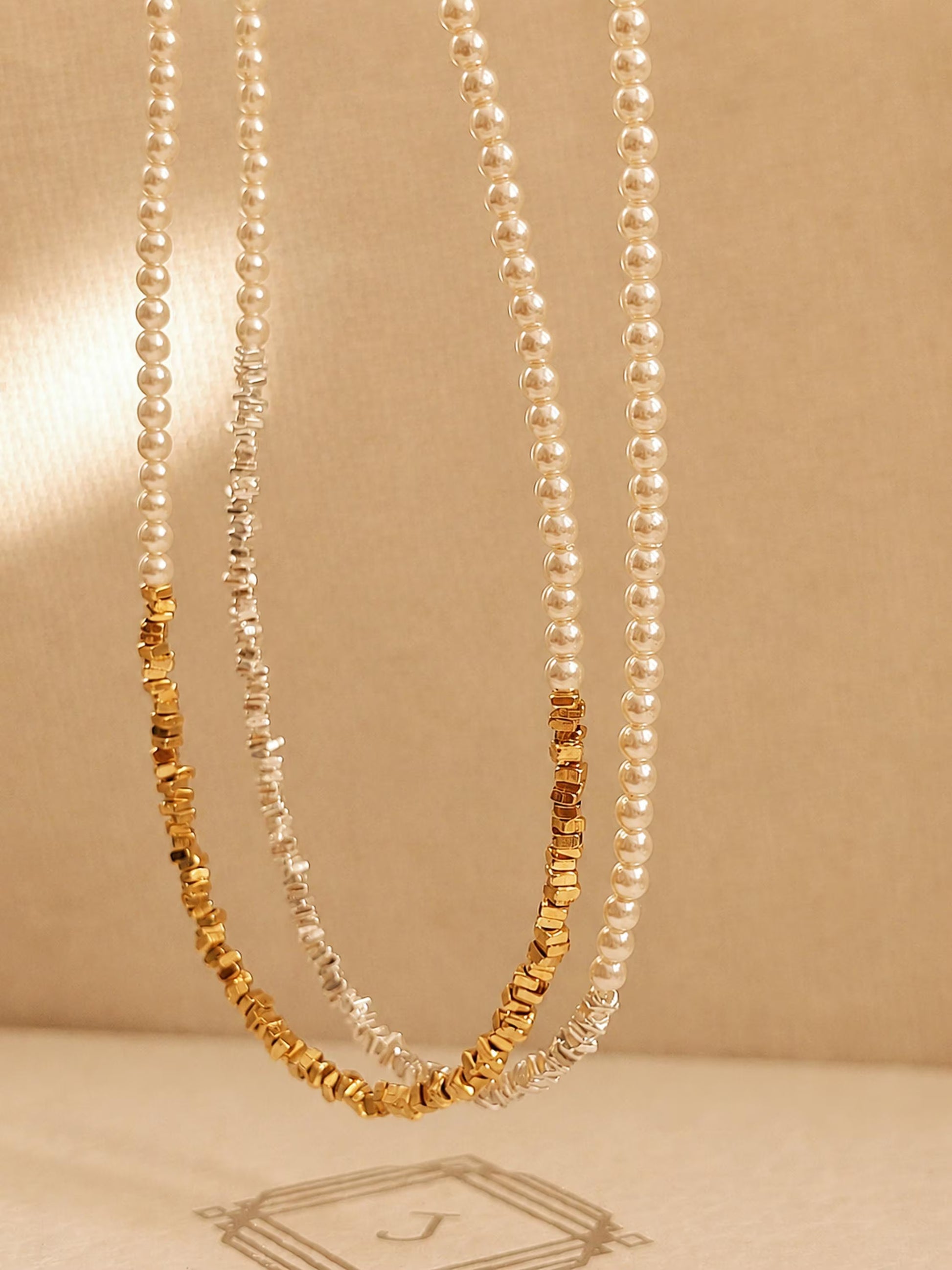 Two dainty 2mm glass pearl choker necklaces displayed on a decorative stone tile, one featuring textured 18k gold-plated nuggets and the other with sterling silver nuggets.