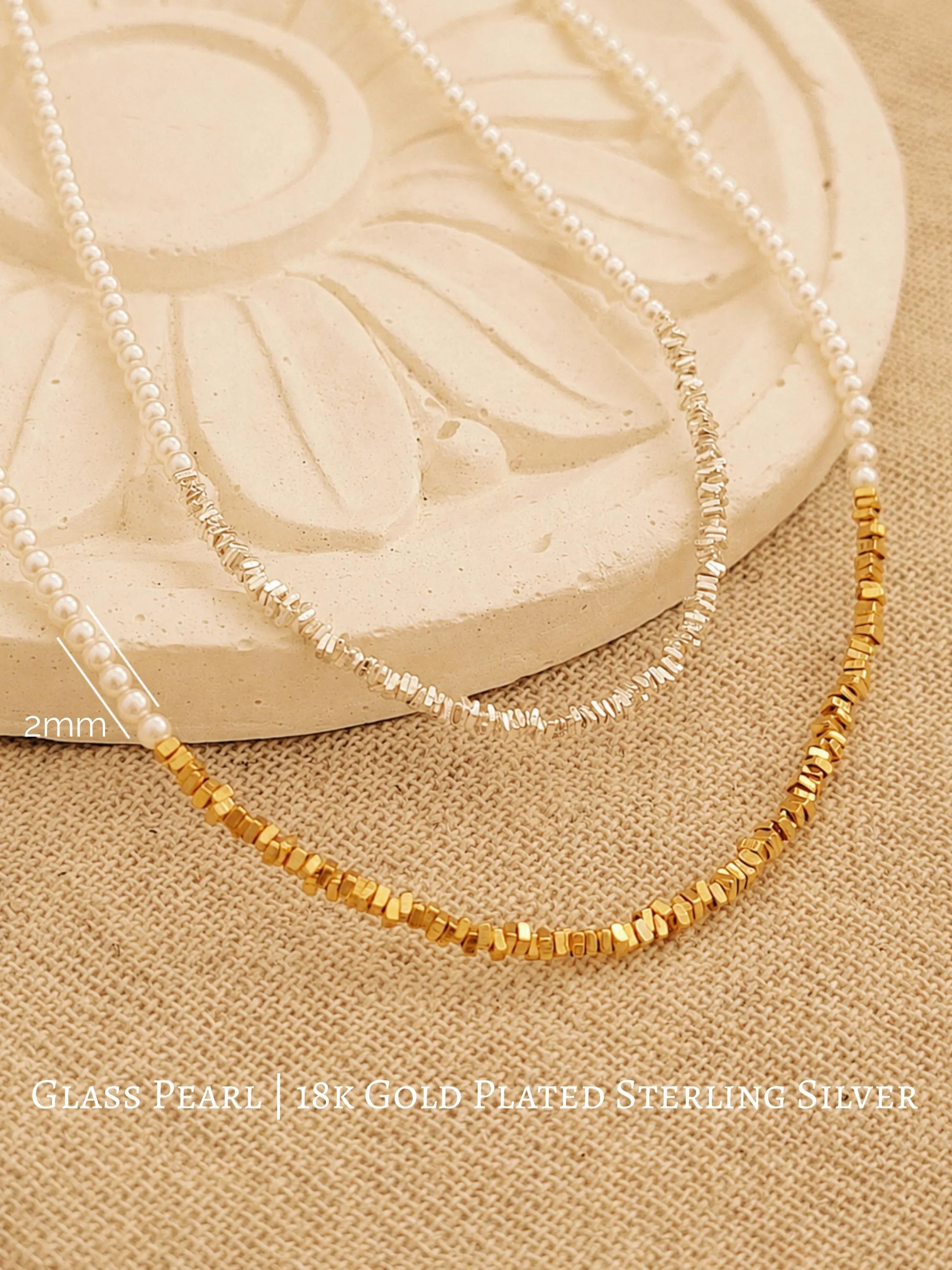 Two dainty 2mm glass pearl choker necklaces displayed on a decorative stone tile, one featuring textured 18k gold-plated nuggets and the other with sterling silver nuggets.