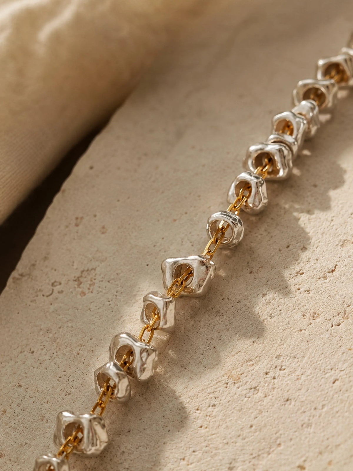 Close up of a mixed metal bracelet featuring two tone with gold and silver on a textured beige surface