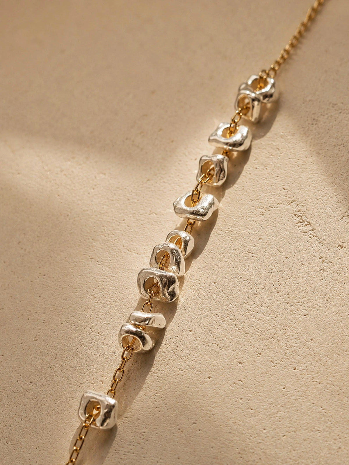 Close up of the organic shaped sterling silver nuggets on a gold chain, dainty mixed metal bracelet.