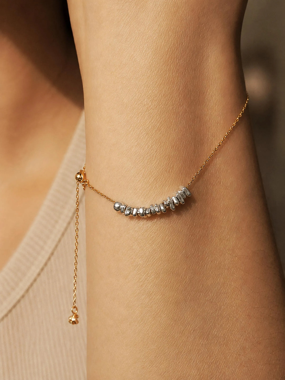 Organic sterling silver beads on a gold chain worn on a wrist against a neutral background
