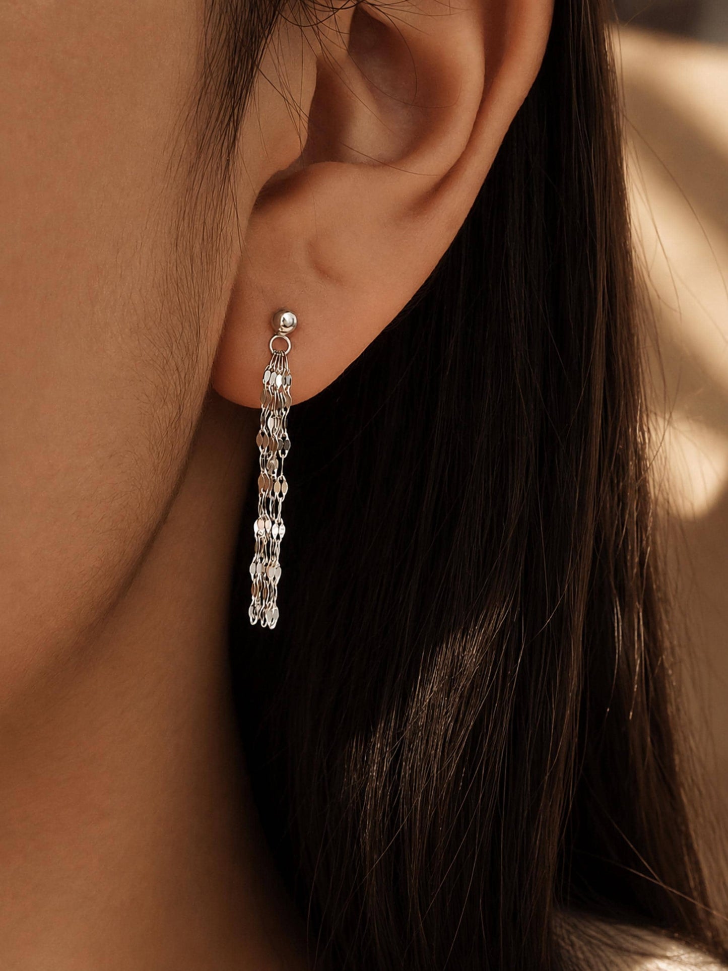 Close-up of a model wearing a delicate sterling silver tassel earring, showing how the shimmering flat-link fringe chains drape and catch the light for an elegant everyday look.