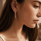 Model wearing a delicate sterling silver tassel earring featuring multiple fine, shimmering flat-link chains that drape elegantly from a classic silver ball stud.