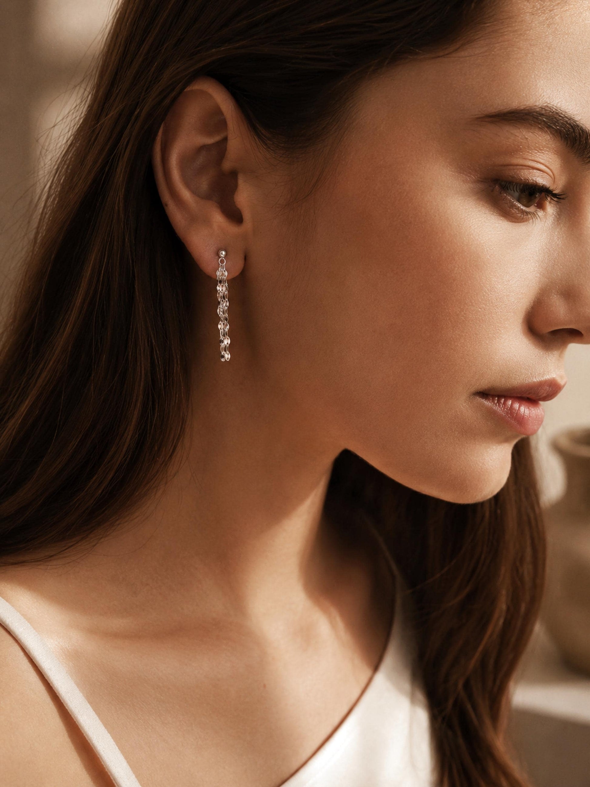 Model wearing a delicate sterling silver tassel earring featuring multiple fine, shimmering flat-link chains that drape elegantly from a classic silver ball stud.