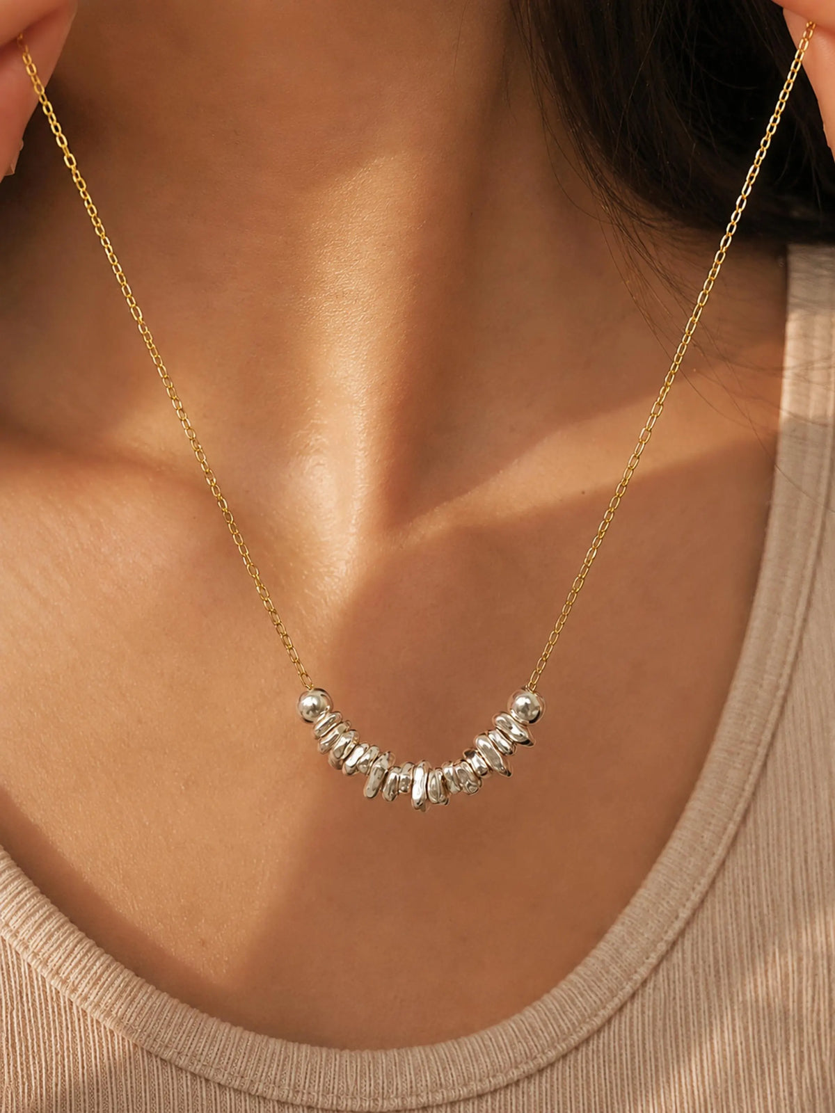 Woman wearing a delicate gold chain necklace with organic sterling silver nugget beads arranged along the neckline.