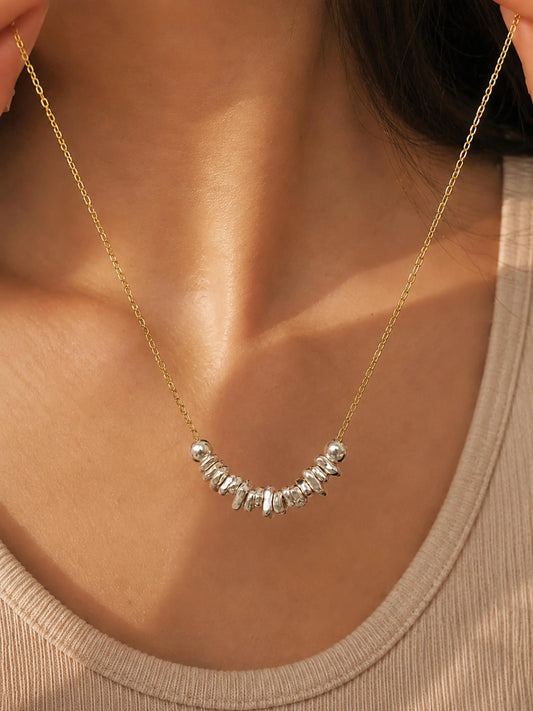 Woman wearing a delicate gold chain necklace with organic sterling silver nugget beads arranged along the neckline.