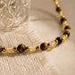 A luxury and dainty beaded necklace made of warm brown tiger's eye and light yellow citrine beads with gold accents displayed on a beige colored cloth.