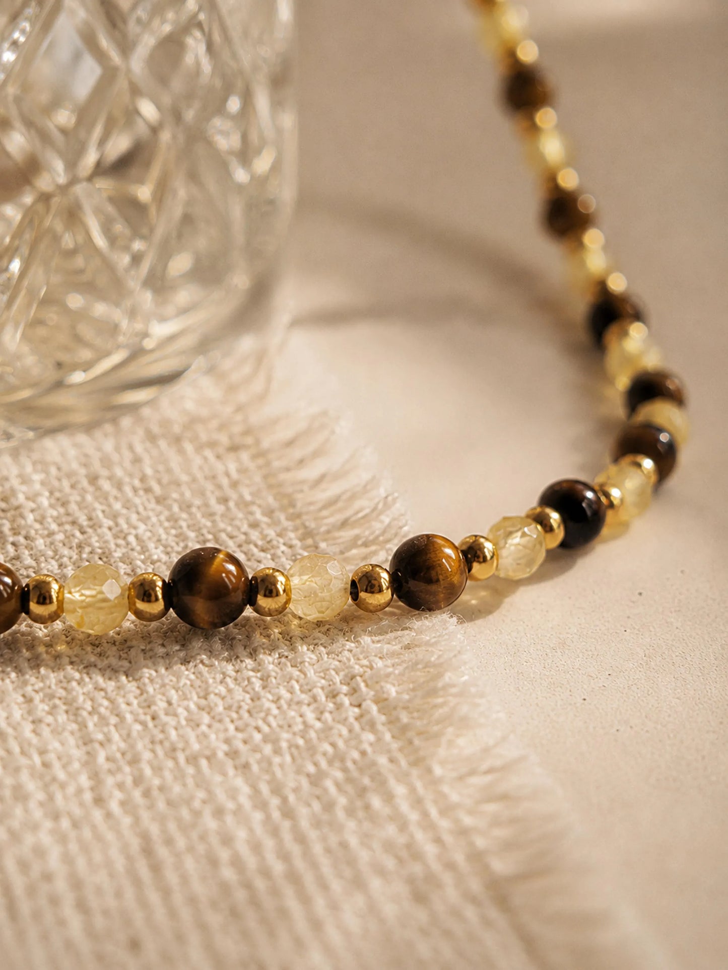 A luxury and dainty beaded necklace made of warm brown tiger's eye and light yellow citrine beads with gold accents displayed on a beige colored cloth.