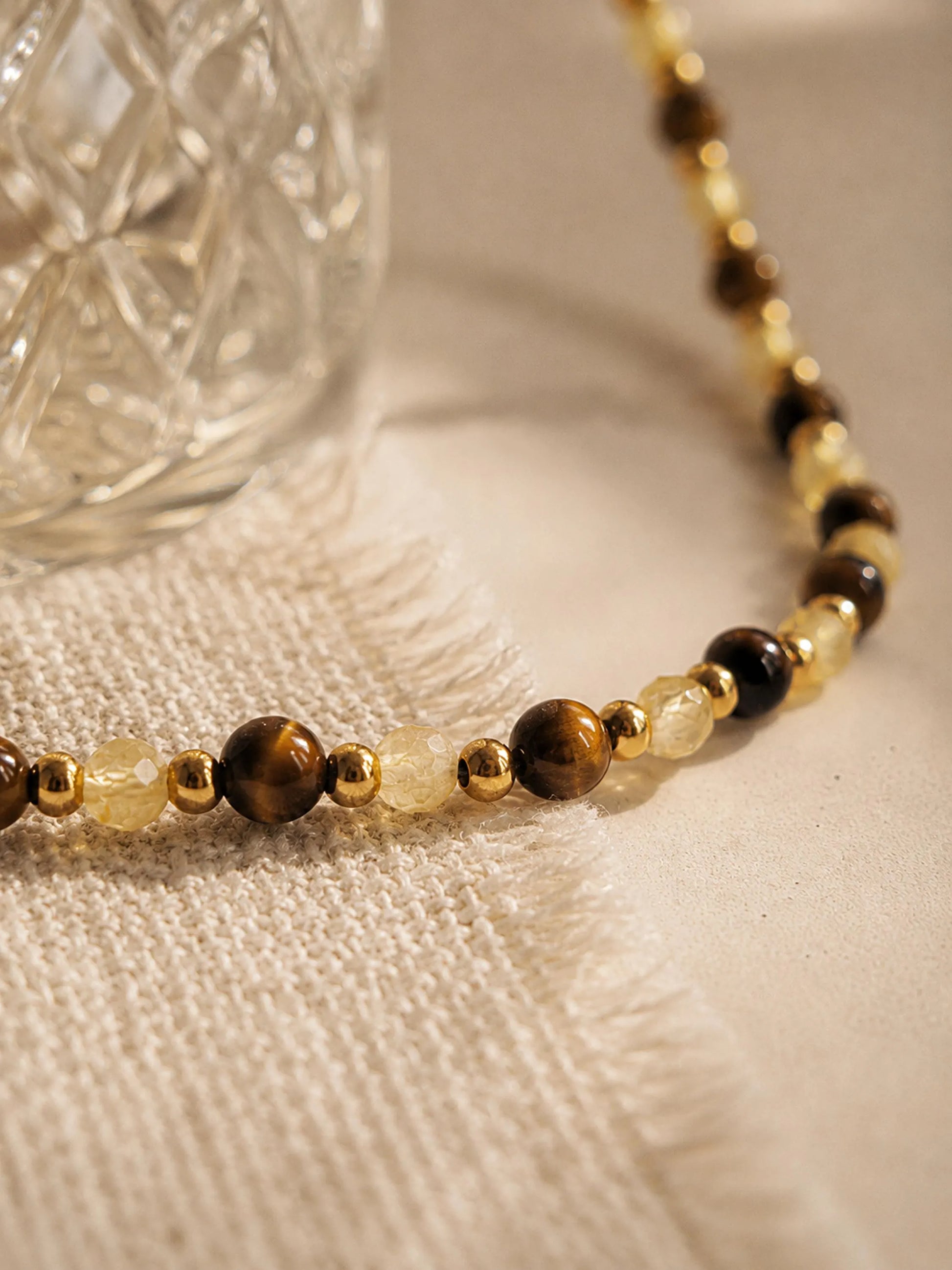 A luxury and dainty beaded necklace made of warm brown tiger's eye and light yellow citrine beads with gold accents displayed on a beige colored cloth.