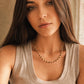 A woman in the photo showcasing a delicate, dainty beaded necklace made of warm brown tiger's eye and light yellow citrine beads. The necklace sits gracefully on the collarbone, styled against a soft beige tank top.