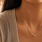 A close-up lifestyle shot of a model wearing a delicate double-strand gold necklace with a small pendant, styled with a beige ribbed top.