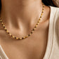 Close-up model photo showcasing a delicate, dainty beaded necklace made of warm brown tiger's eye and light yellow citrine beads. The necklace sits gracefully on the collarbone, styled against a soft beige tank top.