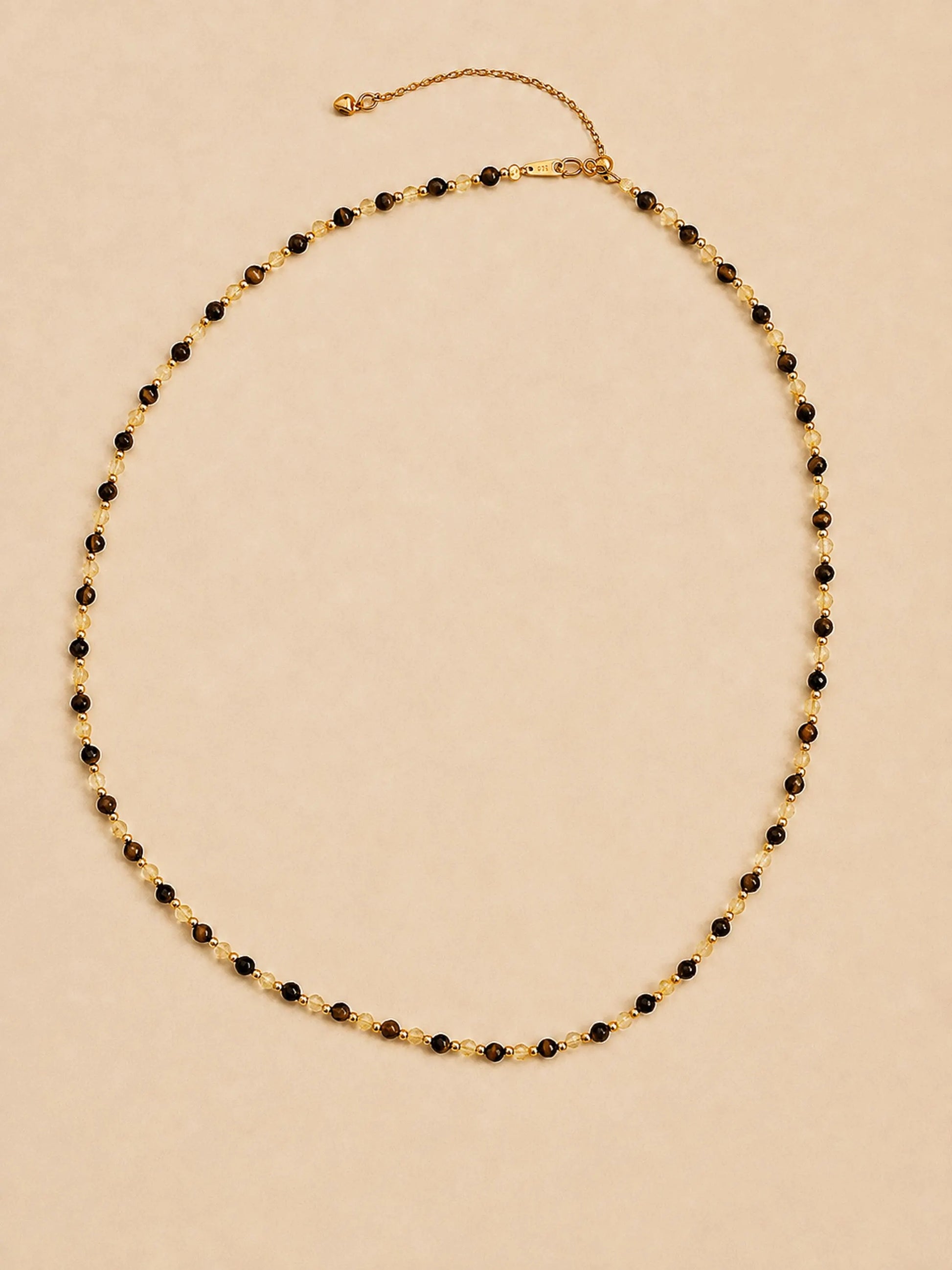 A luxury and dainty beaded necklace made of warm brown tiger's eye and light yellow citrine beads with gold accents displayed on a beige colored surface.