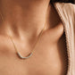 Minimalist sterling silver bead necklace worn on a woman's neckline with a soft beige top and delicate gold chain.