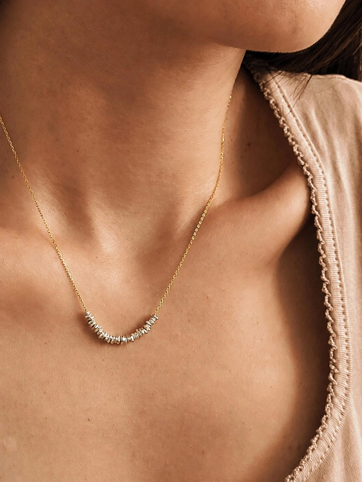 Minimalist sterling silver bead necklace worn on a woman's neckline with a soft beige top and delicate gold chain.