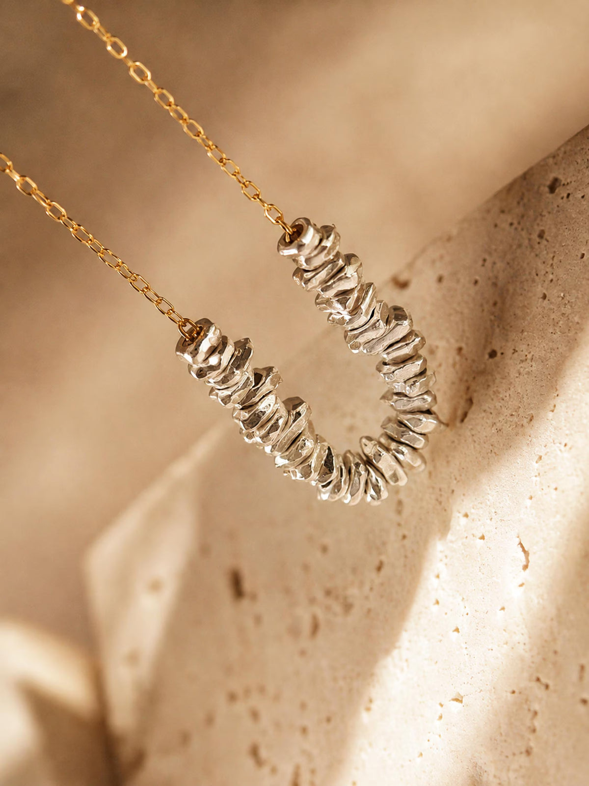 Close-up of irregular sterling silver beads on a fine gold chain, showing the sculptural shapes and polished mixed-metal finish.