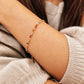 A delicate gold chain bracelet with small colorful crystal beads worn on a girl's wrist, shown in a close-up lifestyle shot with a ribbed beige sweater.