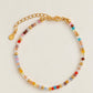 A rainbow colored natural crystal beaded bracelet with 18k gold accents displayed on a light beige background.