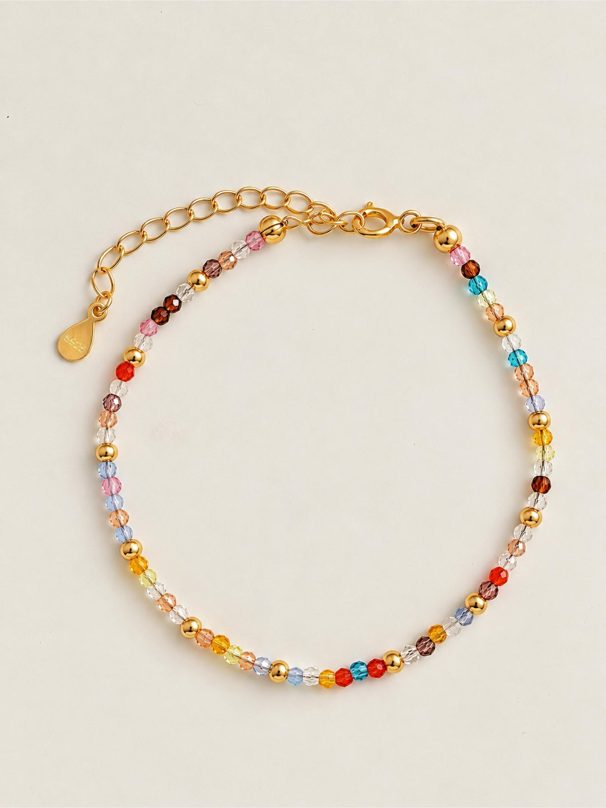 A rainbow colored natural crystal beaded bracelet with 18k gold accents displayed on a light beige background.