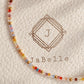 A close-up of a delicate beaded strand with small multicolored crystal beads, laid on textured cream packaging printed with the brand name Jabelle.