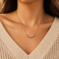 Woman wearing an organic sterling silver bead necklace with a gold chain and a neutral cream V-neck jumper.
