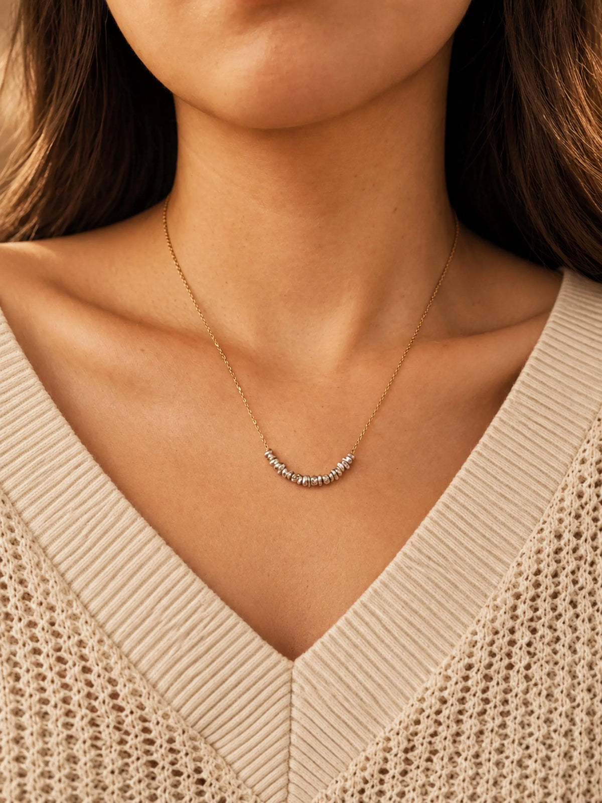 Woman wearing an organic sterling silver bead necklace with a gold chain and a neutral cream V-neck jumper.