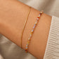 A close-up of a woman's wrist wearing two delicate bracelets: a thin gold bangle and a beaded bracelet with small multicolored faceted crystal beads.