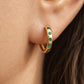 A close-up of a gold hoop earring adorned with small round green gemstones, worn on a woman's ear.