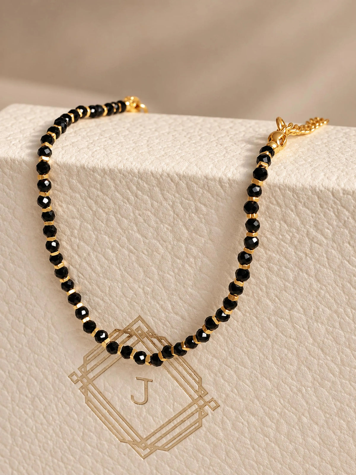 A dainty black onyx beaded bracelet with gold vermeil accents, displayed on a textured JaBelle Jewellery box.