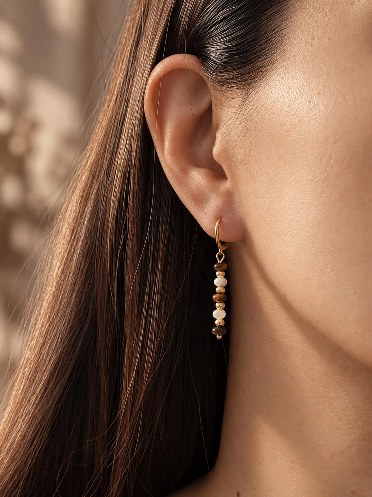 Side profile view of a model wearing delicate Tiger's Eye gemstone drop earrings.