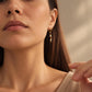 Model wearing handcrafted Tiger's Eye and Mother of Pearl gold drop earrings paired with a beige outfit.