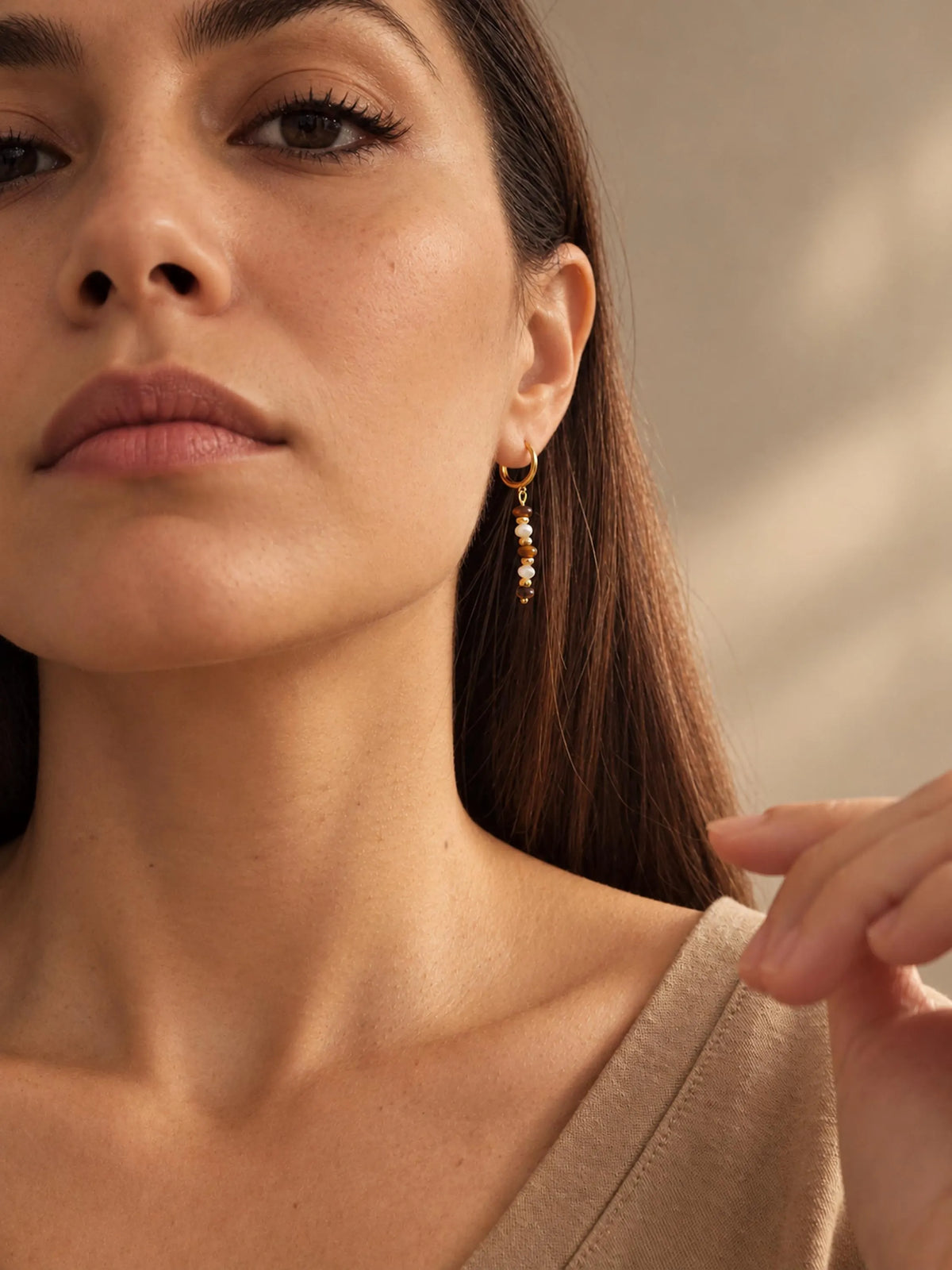 Model wearing handcrafted Tiger's Eye and Mother of Pearl gold drop earrings paired with a beige outfit.