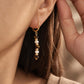 Model wearing a Tiger's Eye and Mother of Pearl gold huggie hoop earring close to the ear.