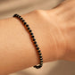 Close-up of a black beaded gemstone bracelet with small gold spacer beads worn on a woman's wrist against a warm beige background.