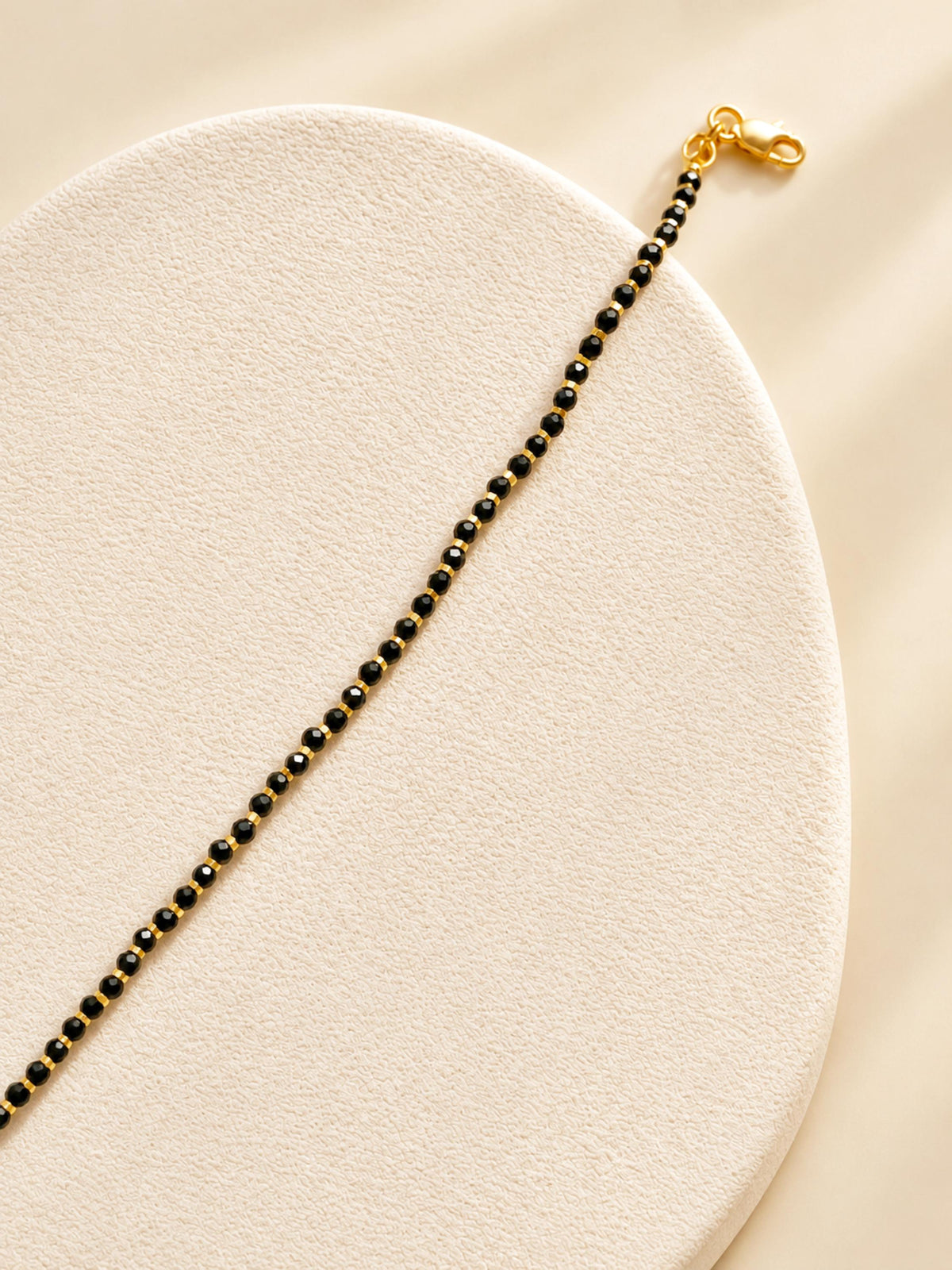 Close-up wrist view of a dainty black onyx bracelet with tiny faceted black beads and subtle gold accents.