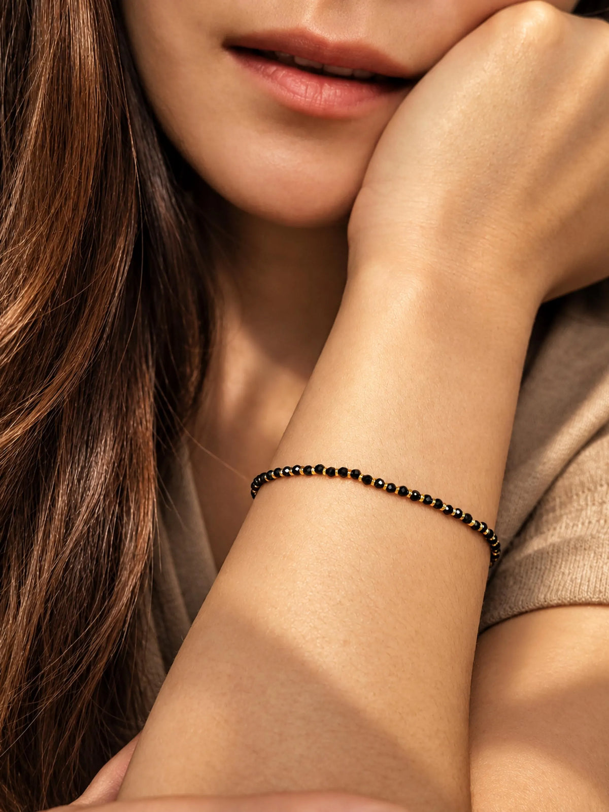 A close-up lifestyle shot of a woman wearing a delicate black onyx beaded bracelet with gold vermeil beads on her wrist.