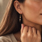 Model wearing handcrafted Tiger's Eye and Mother of Pearl gold drop earrings paired with a beige outfit.