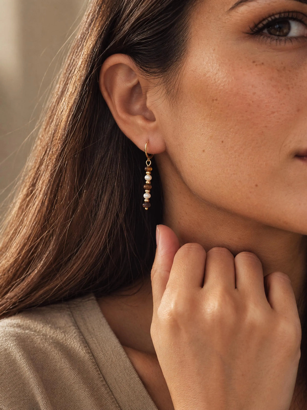 Model wearing handcrafted Tiger's Eye and Mother of Pearl gold drop earrings paired with a beige outfit.
