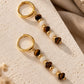 Detailed close-up view of two gold hoop earrings with Tiger's Eye and Mother of Pearl bead dangles.