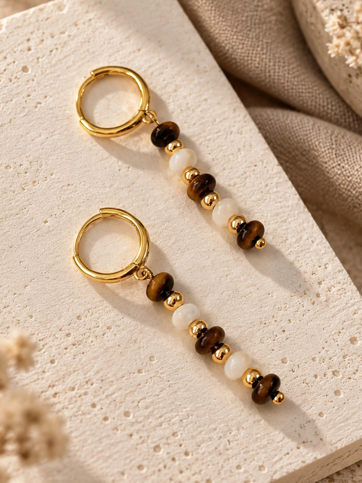 Detailed close-up view of two gold hoop earrings with Tiger's Eye and Mother of Pearl bead dangles.