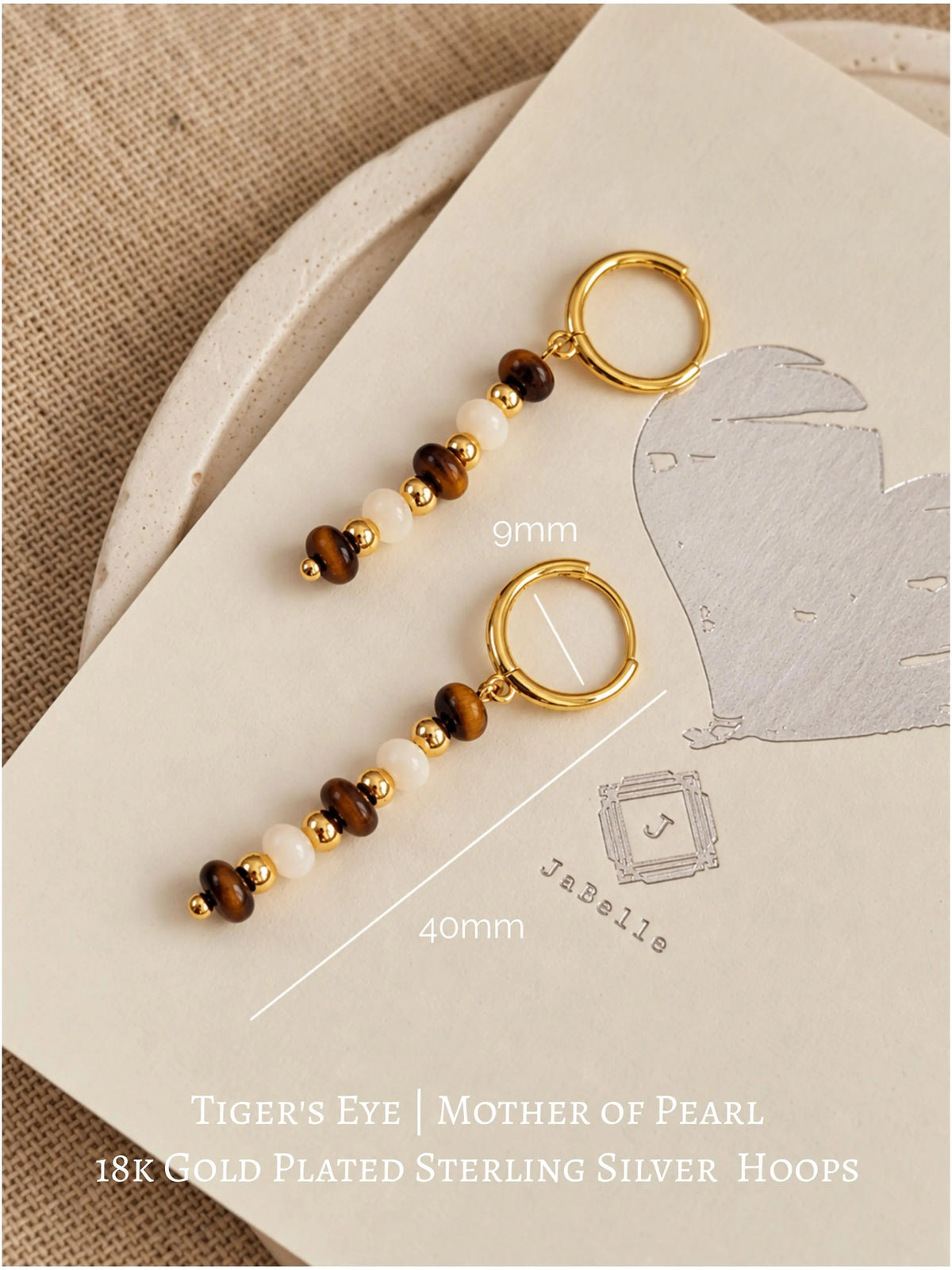Flatlay of Tiger's Eye and Mother of Pearl beaded drop earrings shown on JaBelle logo packaging with size dimensions.