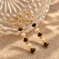 Tiger's Eye and Mother of Pearl beaded gold drop earrings displayed on a ribbed glass bowl and linen surface.