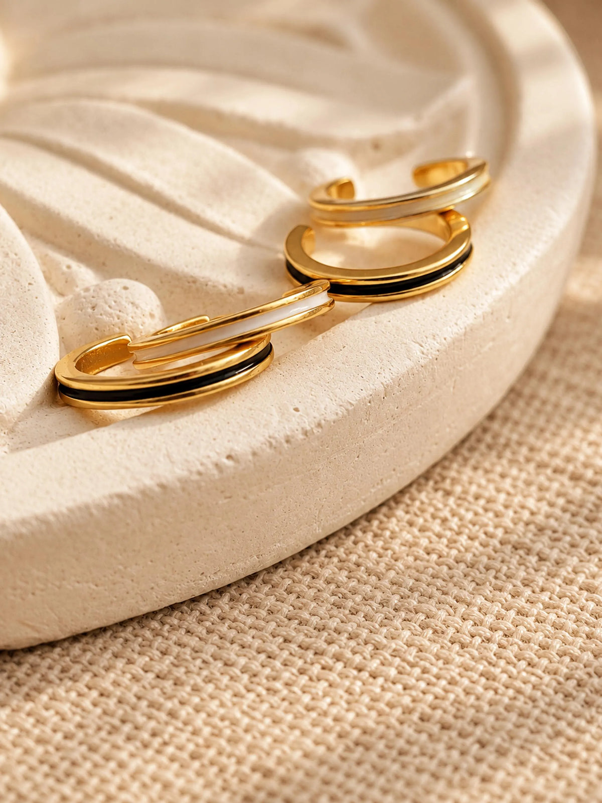 Black and white enamel gold ear cuffs displayed together on a soft neutral jewellery tray.